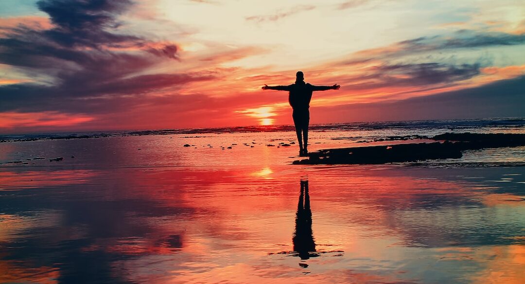 silhouette of person standing on rock surrounded by body of water