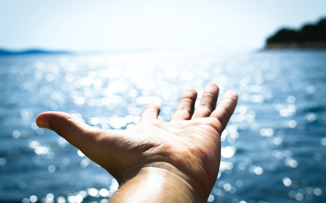 person hand reaching body of water