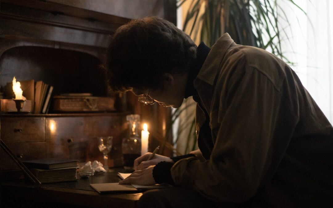 focused man writing on paper beside a candlelight